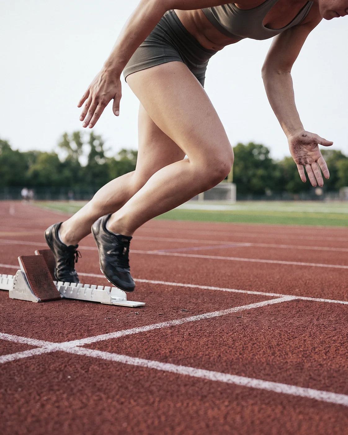 A sprinter driving out of the starting blocks on a red running track, seen low from the side