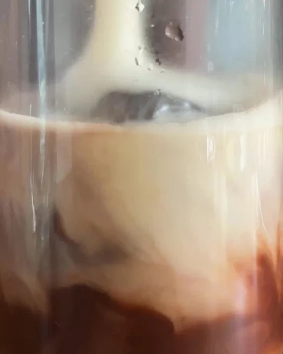 Milk poured over ice into a tall glass of cacao