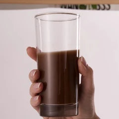 A hand holding a tall glass of Thunder Honey made in the glass bottle