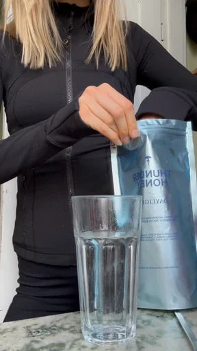 A scoop of Thunder Honey going into a tall glass of cold water, the Daylight pouch held up behind it