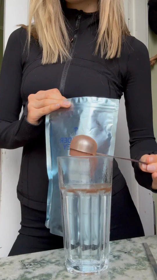 A heaped steel scoop of Thunder Honey lowered into a tall glass of cold water, the Daylight pouch held open behind it