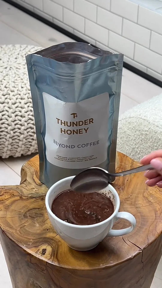 A spoon lifting hot Thunder Honey from a white cup on a wooden stump, a pouch of Thunder Honey standing behind it